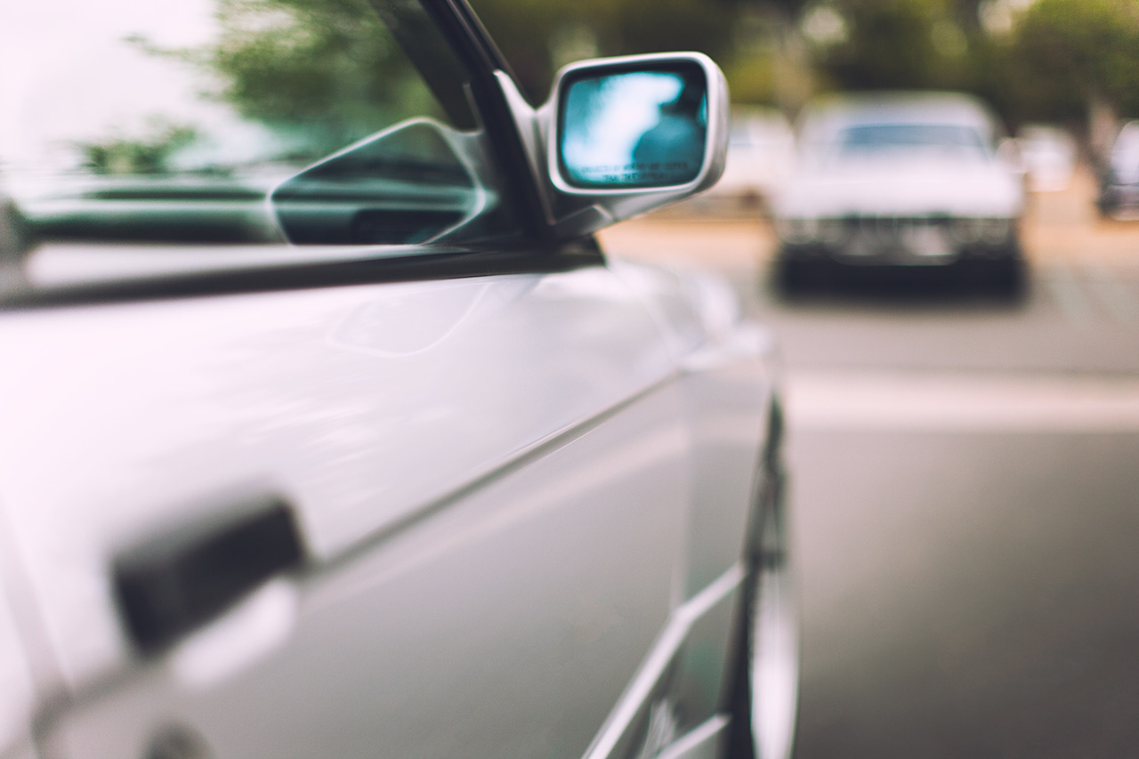 Silver BMW E30 M3 parked across from a classic ancestor